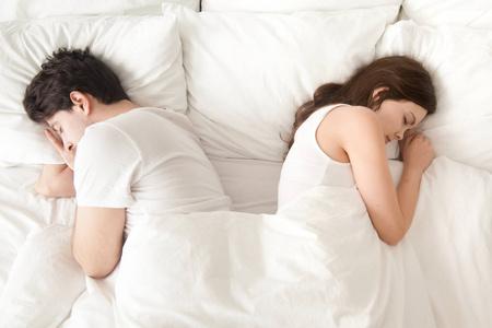 感情破裂的夫妻睡觉背靠背在家里的床上照片